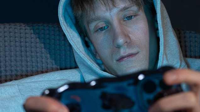 Sinisävyisessä kuvassa vakavailmeinen nuori mies katsoo kännykkäänsä.