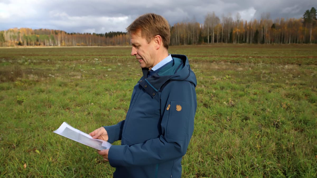 Lahden kaupungingeodeetti Juha Helminen Koivistoisen mansikkapellon laidalla katsoo kädessään olevaa paperia, pelto taustalla.