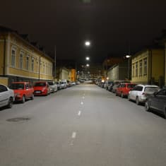 Tyhjä katu yöllä. Autoja on parkkeerattu kadun varrelle.