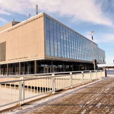 Pyörätien silta, jossa valkeat metallikaiteet. Taustalla betoninen talo, jonka seinässä teksti TEATTERI.