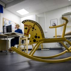 Leikkihevonen neuvolan lattialla hoitaja työskentelee taustalla.