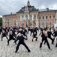 Yli sata mustiin pukeutunutta nuorta tanssijaa esittämässä Kuopio tanssii ja soi -tapahtuman avajaisesitystä Kuopion torilla kaupungintalon edessä.