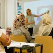 Opettaja näyttää taululta kellonaikoja ja oppilaat katsovat