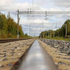 Rautatien kiskon pinnasta kuvattu näkymä junanradalle, radan yläpuolella sähköjunien kulkujohtimia.