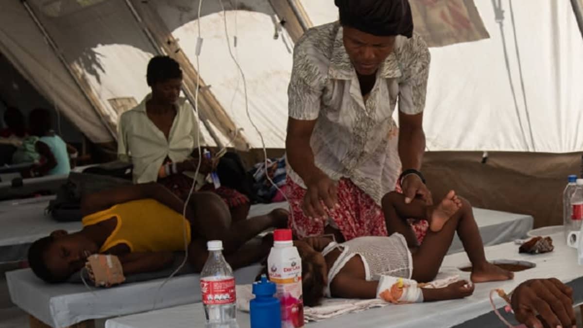 Nestetytettäviä kolerapotilaita makaamassa vuoteilla teltassa. Keskimmäisenä pieni lapsi, jonka ylle on kumartunut nainen.