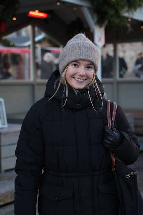 Ung kvinna med vinterjacka och yllemössa på julmarknad. 