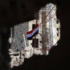 Syyrian lippu liehuu raunioissa.