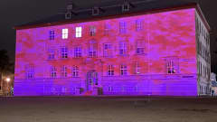 Punasävyinen abstrakti valoteos ison koulurakennuksen seinällä. 