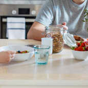 Aamiaspöydässä on mysliä ja mansikoita, pieni lapsi katsoo vanhempaansa kohti.
