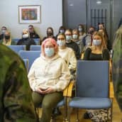 Nuoria naisia istumassa luokkahuoneessa, jossa maastopukuiset puhuvat.