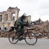 Henkilö pyöräilee tuhoutuneen rakennuksen vieressä.
