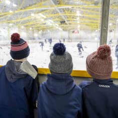 Pojat katsovat kaukalon laidalla juniorien jääkiekkoharjoituksia.