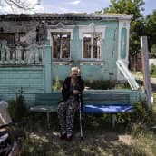 Vanha nainen istuu penkillä pommitusten vaurioittaman talon edustalla.