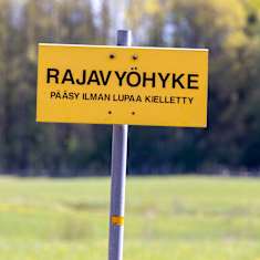 rajavyöhykkeestä kertova kyltti pellon laidassa.
