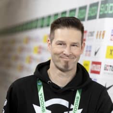 Darude, a man in his 40s, with short hair and a small beard, wearing a black hoodie and grinning