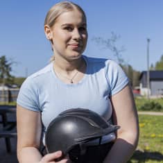 Hilda Merivirta pitää kädessään ratsastuskypärää ja katsoo kameraan Heponiityn ratsastustilalla. 