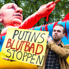 Putinia esittävä nukke kylpee veressä. Mies pitelee saksankielistä kylttiä.