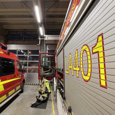 Palolaitoksen kaksi autoa sisällä hallissa, niiden välissä palomiehen varusteet valmiina hälytystä varten.