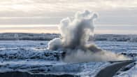 Smoke and dust rising from an explosion in an open-pit mining area with snow on the ground and trees in the distance.
