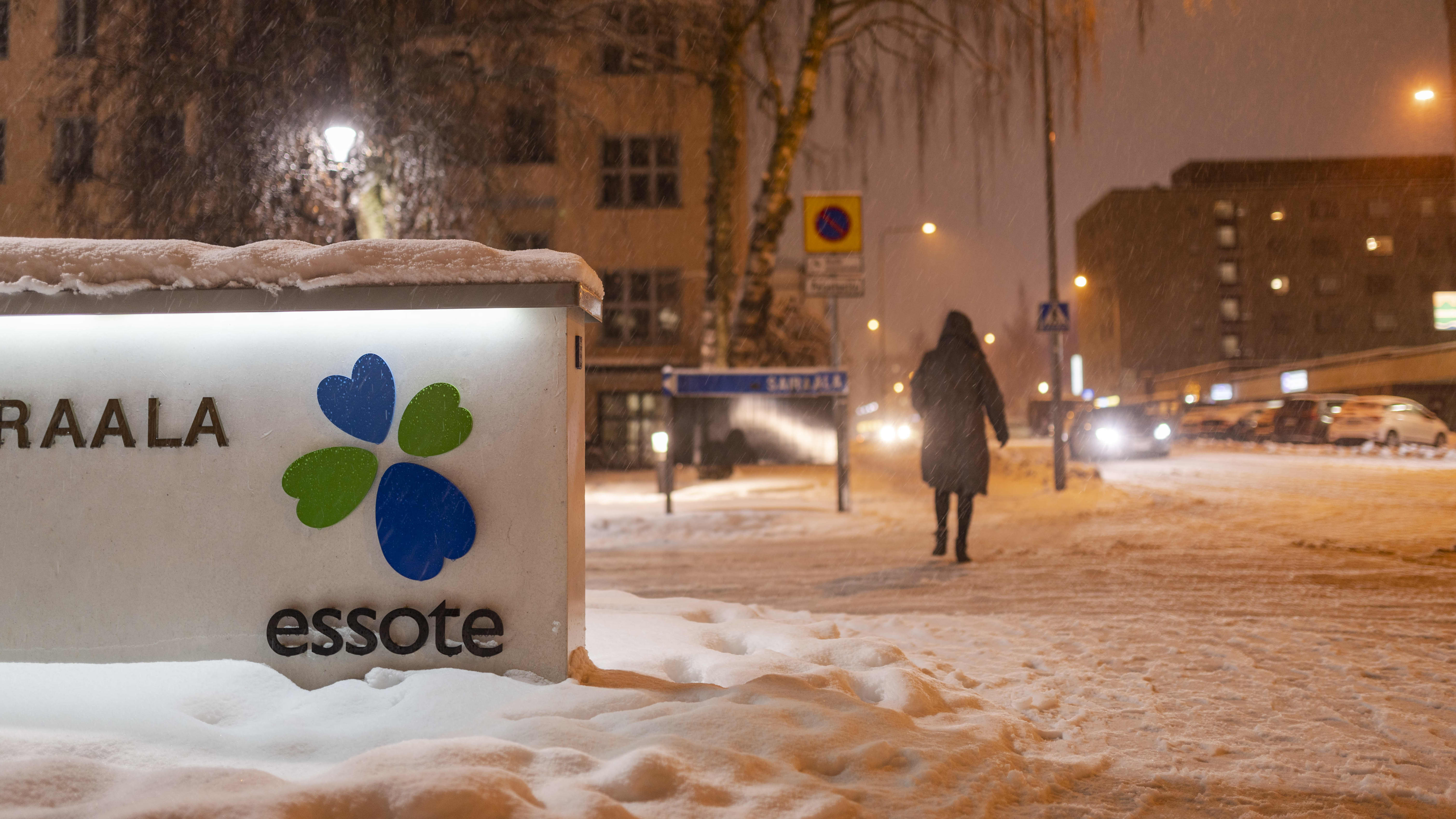 Talvinen maisema Mikkelin keskussairaalan edustalla. Henkilö kävelee kauemmaksi kamerasta lumisateessa. Edustalla kuntayhtymä Essoten kyltti.
