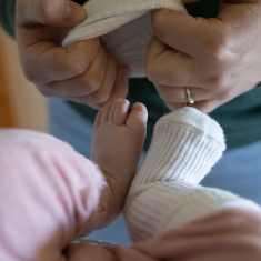 A woman putting a sock on a baby's foot.