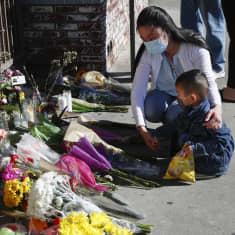 Nainen ja lapsi maahan asetettujen kukkien edessä Monterey Parkin joukkoampumisen uhrien muistopaikalla.