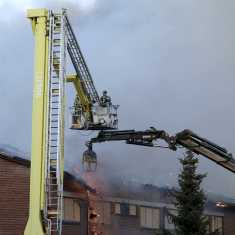 Brandmän står i en lyftkran och släcker ett tak som brinner.