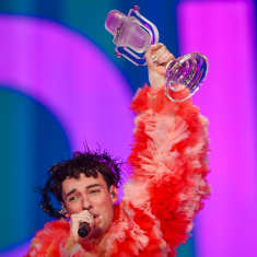 Nemo puhuu mikrofoniin lavalla pitäen ylhäällä Euroviisu pokaalia.