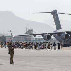  Flygfältet i Kabul. En folksamling framför en Air Force Boeing C-17. Soldater övervakar.