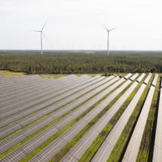 Aurinkopaneeleita aurinkopuistossa. Taustalla näkyy tuuliturbiineja. Solarigo Systems Oy:n aurinkopuisto Kalajoella Pohjois-Pohjanmaalla.