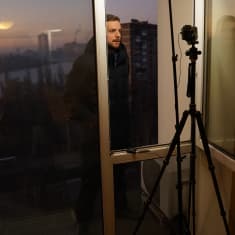 Ylen Moskovan-kirjeenvaihtaja Erkka Mikkonen tekee tv-suoraa hotellihuoneessa. Mikkonen seisoo ikkunalaudalla ja taustalla näkyy hämärä kaupunki..