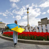 Ihmisiä Itsenäisyyden aukiolla Kiovassa 1. toukokuuta. Etualalla nuori nainen Ukrainan lippu hartioillaan. 