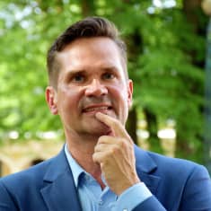 Mika Aaltola katsoo suoraan kameraan Porin Raatihuoneenpuistossa käsi leualle aseteltuna.