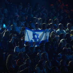 Yleisön keskellä joku pitää ylhäällä Israelin lippua.