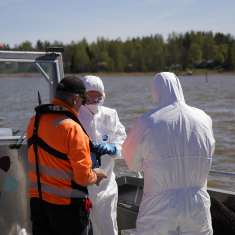 Två personer i skyddskläder och en person med flytväst ombord en båt med Borgås logo.