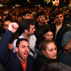 Väkijoukko osoittaa mieltään aukiolla illan pimentyessä. Etualalla mustahiuksinen mies huutaa ja heristää kättään ilmassa.