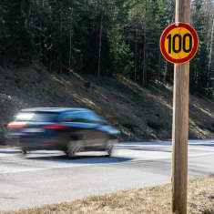 Personbil på landsväg. I förgrunden en skylt med hastighetsbegränsningen 100 kilometer i timmen.