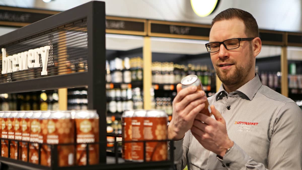 Kauppias Juha Jylli tutkii tölkkiä oluthyllyjen välissä 