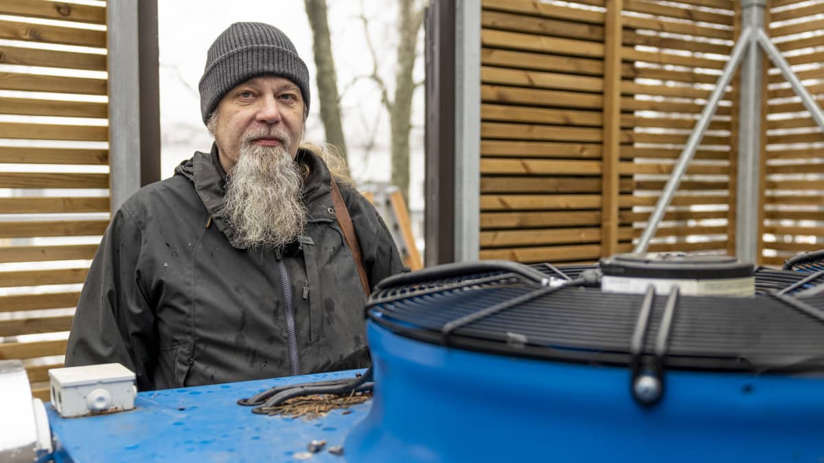 Taloyhtiön puheenjohtaja Risto Lähteenmäki seisoo lämmön talteenottoyksikön ja rimaseinän välissä.
