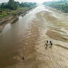 Aerial view of a mostly-dry riverbed, with small silhouettes of four people and a dog walking on the sand with vegetation in the riverbanks.  