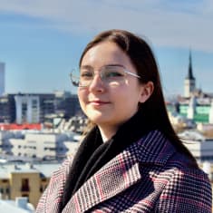 Silmälasipäinen nuori tummatukkainen nainen katsoo kameraan taustallaan Tallinnan kaupunki.