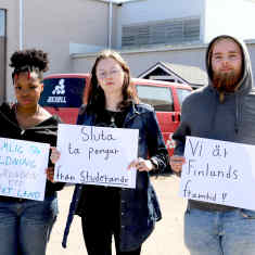 Tre studerande vid Axxell i Pargas håller upp protestskyltar i händerna mot regeringens nedskärningar. 