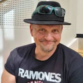 Klamydia-bändin laulaja Vesku Jokinen istuu portailla hattu päässään ja hymyilee.
