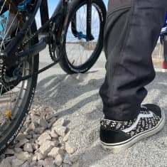 Lähikuva polkupyörää muistuttavan BMX-pyörän renkaasta ja ajajan jalasta. Kuskilla jalassaan mustavalkoiset tennarit.