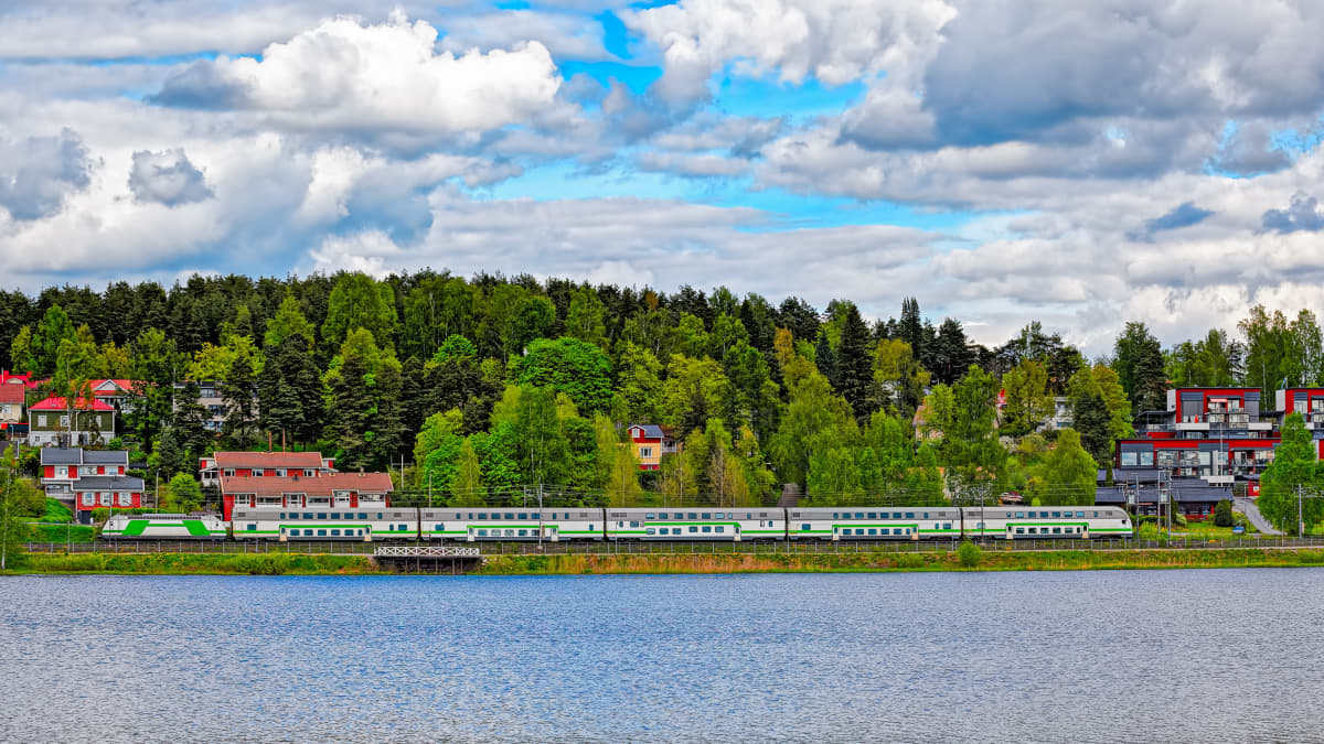 Kuva suomalaisessa maisemassa kulkevasta junasta. Metsää takana, vettä edessä. 