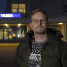 Mies katsoo tuimasti kameraan, taustalla Lapin keskussairaalan "LKS Vilkka" -kyltti.