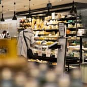 Henkilö kumartuu katsomaan juustoja kylmäaltaasta Stockmannin Herkku-ruokakaupassa.