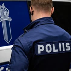 Anonyymi poliisi kuvattu takaa päin poliisiauton edessä.