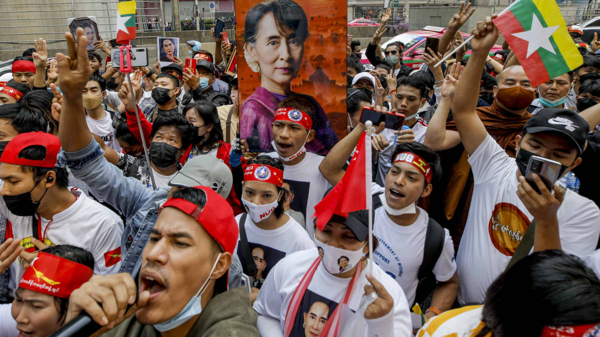Joukko ihmisiä kohottaa lippuja ja kantaa Aung San Suu Kyin kuvaa.