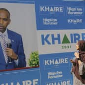 Somalialainen hunnutettu nainen katsoo läheltä suurta sinisävyistä vaalimainosta, jossa suurena siniseen pukuun ja siniraidalliseen kravattiin pukeutunut presidenttiehdokas Ali Khaire. 